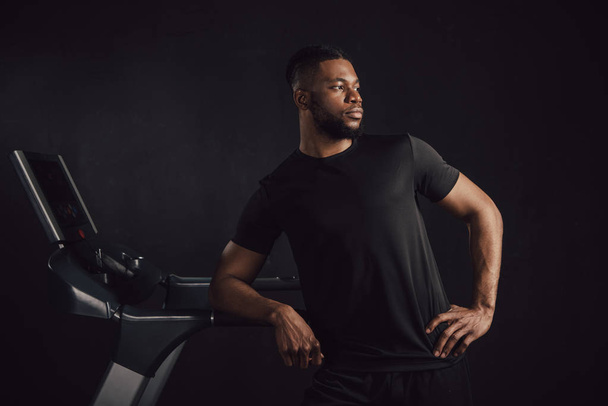 sportos fiatal afroamerikai férfi hajlik a futópad és látszó el elszigetelt a fekete - Fotó, kép