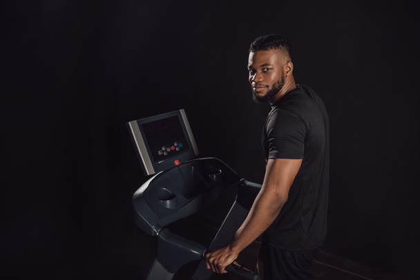 young african american sportsman exercising on treadmill and looking at camera isolated on black - Foto, Bild