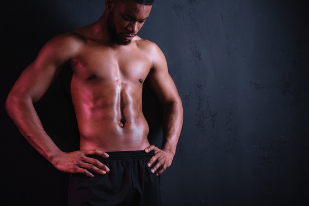 muskulöser Mann mit nacktem Oberkörper, der mit den Händen auf der Taille steht und auf schwarz herabblickt - Foto, Bild