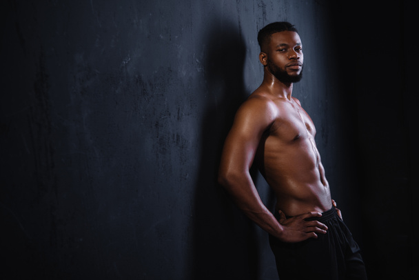shirtless muscular young african american man standing with hands on waist and looking at camera on black    - Fotó, kép