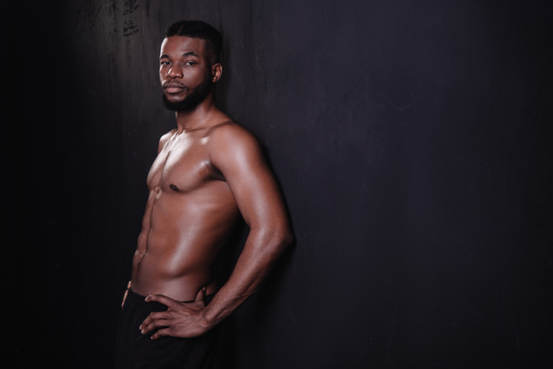 handsome shirtless muscular young african american man looking at camera on black   - Фото, зображення