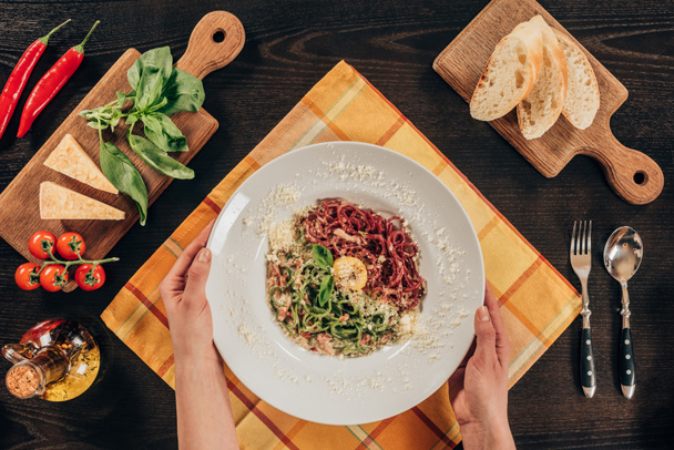 cropped image of woman holding plate with pasta, bacon and parmesan cheese - Valokuva, kuva