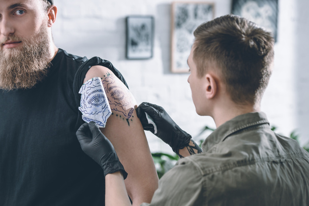 Artista del tatuaje en guantes trabajando en boceto de pieza de hombro en estudio
 - Foto, Imagen