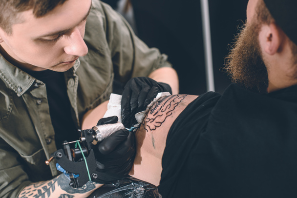 Художник татуювання і бородатий чоловік під час процесу татуювання в студії
 - Фото, зображення