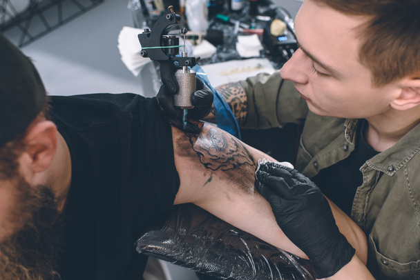 Hombre barbudo y maestro del tatuaje durante el proceso de tatuaje en el estudio
 - Foto, Imagen