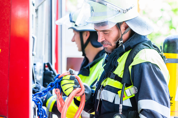 Пожарный проверяет шланги на пожарной машине
 - Фото, изображение