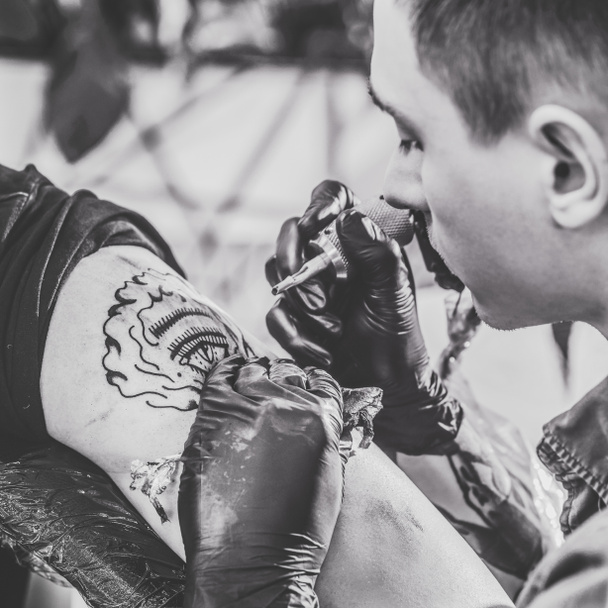 Black and white photo of tattoo master working on shoulder piece in studio - Photo, Image