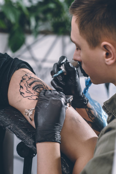 Tattoo artist in gloves working on shoulder piece in studio - Photo, Image
