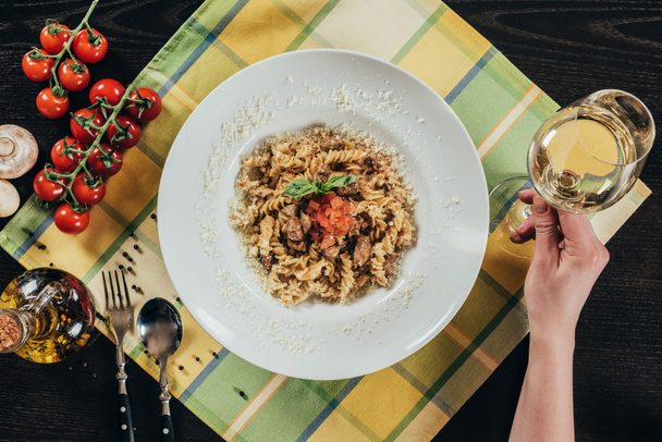 cropped image of woman holding glass of wine near plate with pasta - Valokuva, kuva