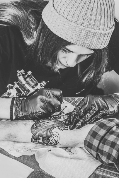 Чорно-біла фотографія художника татуювання жінки в рукавичках, що працюють на руці
 - Фото, зображення