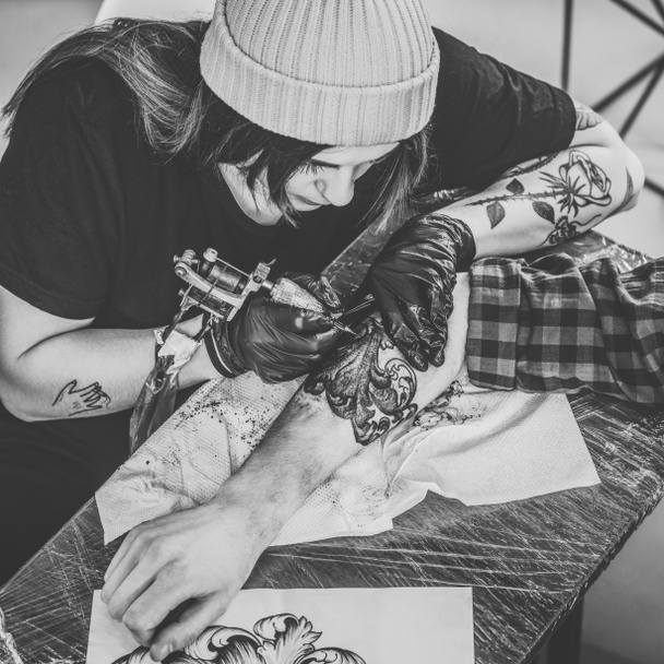Foto en blanco y negro del maestro y el hombre del tatuaje de la mujer durante el proceso de tatuaje en el estudio
 - Foto, Imagen