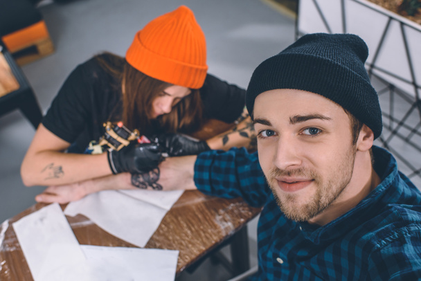 Усміхнений чоловік і майстер татуювання під час процесу татуювання в студії
 - Фото, зображення