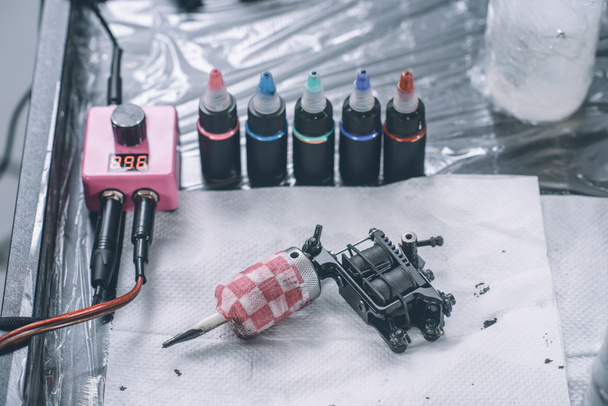 Tatuaje artista lugar de trabajo con máquina y botellas con tinta de tatuaje colorido
  - Foto, Imagen