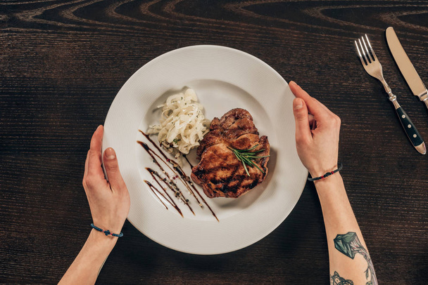 imagen recortada de la mujer sosteniendo el plato con carne de res encima de la mesa
 - Foto, Imagen