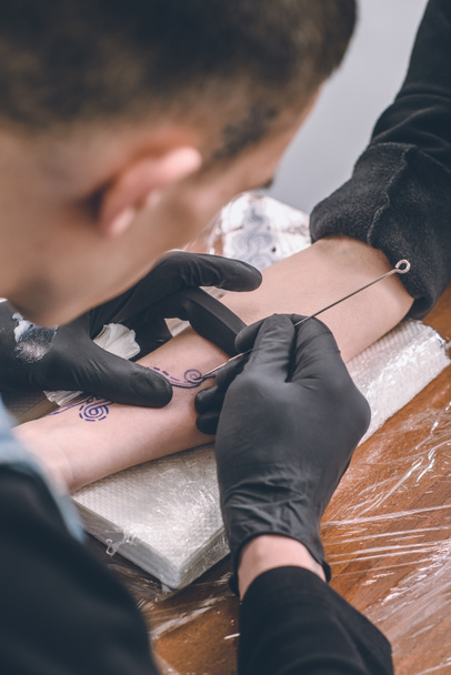 Καλλιτέχνης τατουάζ στα γάντια που εργάζεται σε γυναικείο χέρι κομμάτι στο studio - Φωτογραφία, εικόνα