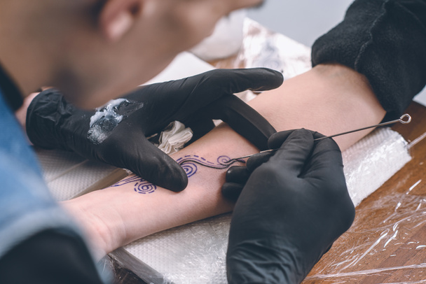 Mies taiteilija käsineissä työskentelee käsivarren pala tatuointi studiossa
 - Valokuva, kuva