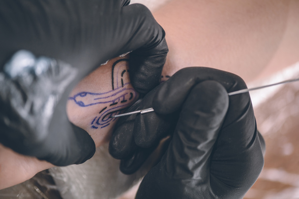Close-Up Nézd tetoválás művész dolgozik a kar darab kesztyű - Fotó, kép