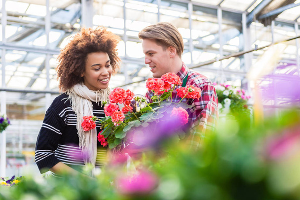 Kaunis nainen ostaa punainen pelargonium neuvoja kukkakauppias
 - Valokuva, kuva