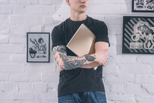 Татуйований чоловік стоїть біля стіни в студії татуювання
 - Фото, зображення