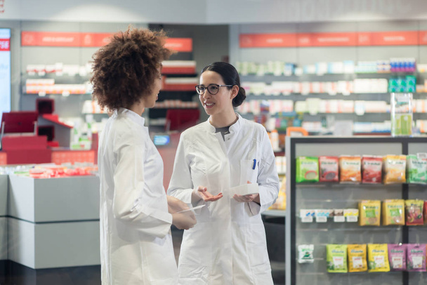 Kaksi ystävällistä kollegaa puhuu työskennellessään yhdessä nykyaikaisessa apteekissa
 - Valokuva, kuva