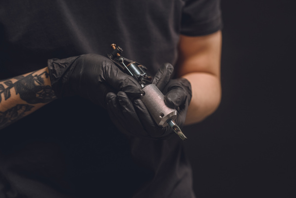 Maestro del tatuaje en guantes que sostienen la máquina de tinta aislada en negro
 - Foto, Imagen
