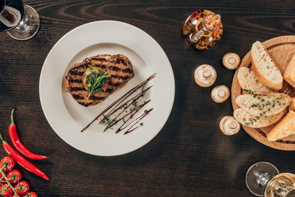 top view of beef steak on plate, mushrooms and baguette on table - Fotó, kép