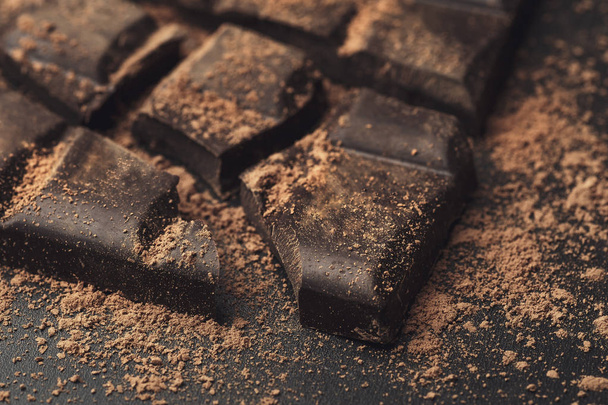 Barre de chocolat cassée en morceaux et poudre de cacao sur fond sombre
 - Photo, image