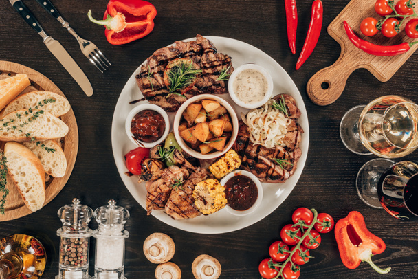 vista superior de prato com bifes de carne, legumes grelhados e vinho na mesa
 - Foto, Imagem