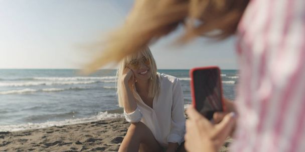 Two Girl Friends Taking Photo with Smartphone On Empty Beach during autumn day - Photo, Image