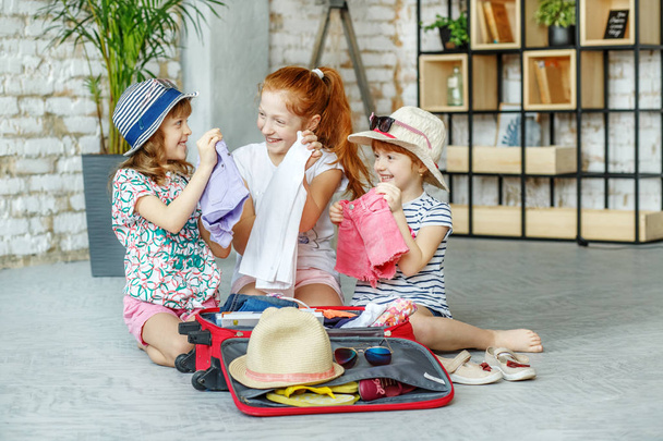 Trzy małe dziewczynki pakowane ubrania w walizce. Koncepcja,  - Zdjęcie, obraz