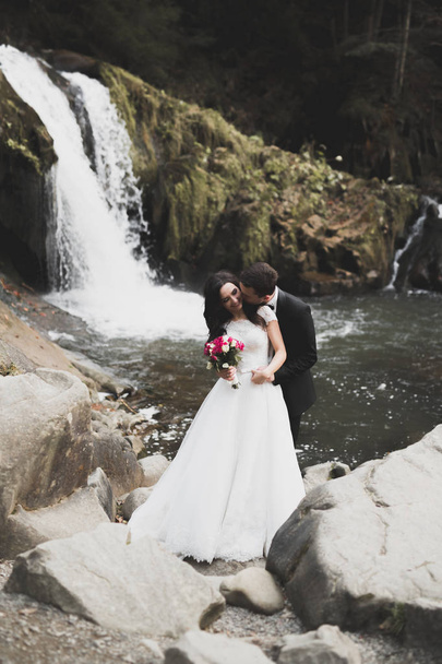 Elegant stylish happy brunette bride and gorgeous groom on the background of a beautiful river in the mountains - Photo, image