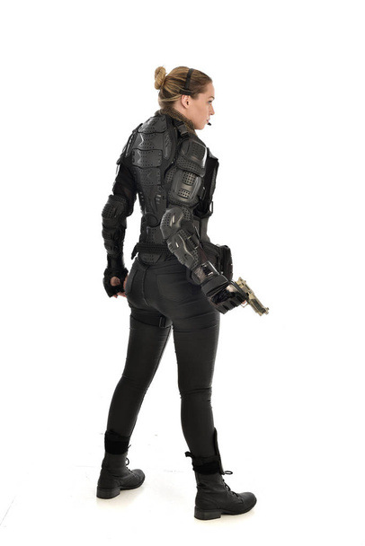 Beyaz stüdyo arka plan üzerinde izole bir silah tutan siyah taktik zırh giyen kadın asker portresi tam uzunlukta. - Fotoğraf, Görsel
