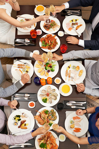 Skupina lidí cinkání sklenic u jídelního stolu s mořskými plody, pohled shora - Fotografie, Obrázek