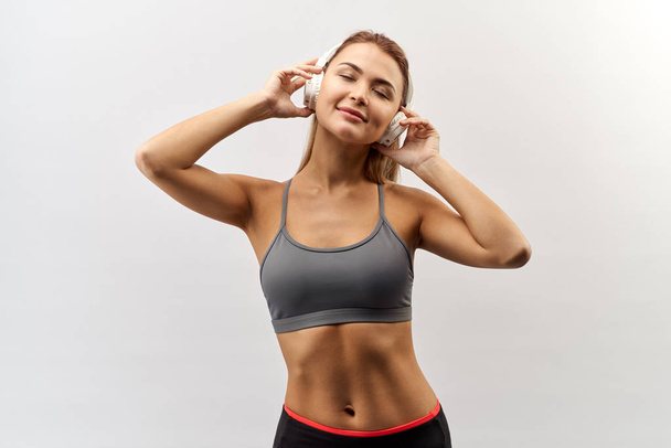 young athletic tanned white-skinned girl in a grey sports top enjoy the music from the headphones on her head - Foto, immagini