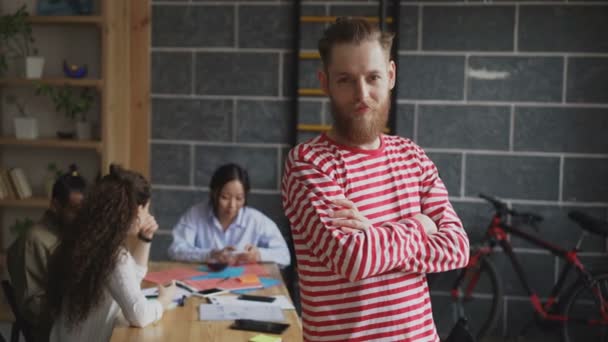 Portrait de jeune entrepreneur masculin hipster souriant et regardant la caméra tandis que ses collègues travaillant au bureau loft moderne
 - Séquence, vidéo