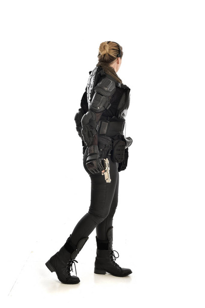 volledige lengte portret van vrouwelijke soldaat het dragen van zwarte tactische armour houdt een pistool, geïsoleerd op witte studio achtergrond. - Foto, afbeelding