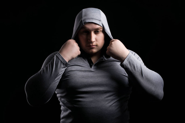 Sports large muscular man in a hood on black background contrast - Фото, зображення