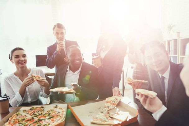 The office staff eat pizza and drink coffee in the business office. - Foto, Bild