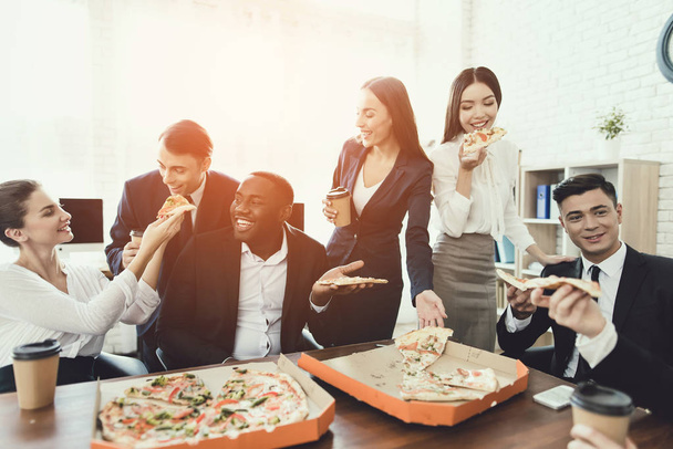 The office staff eat pizza and drink coffee in the business office. - Foto, imagen