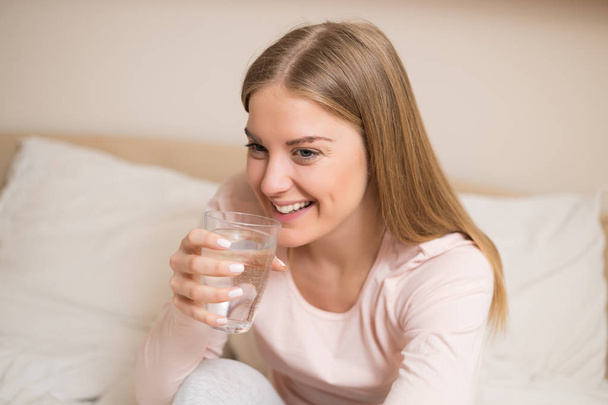 Beautiful woman in pajamas drinking water in the bedroom. - Photo, image