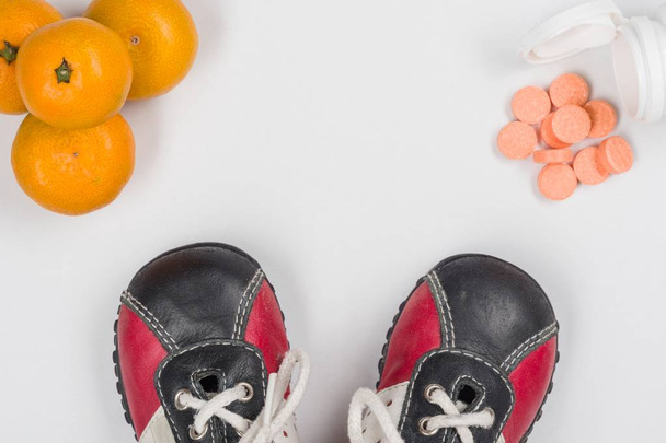 Vitamin C. Natural citrus and synthetic tablets, choice. White background, children's sneakers - 写真・画像