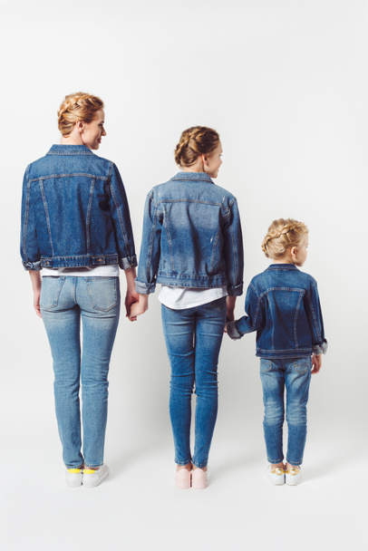 back view of family in similar denim clothing standing in row and holding hands isolated on grey - Foto, afbeelding
