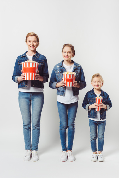 smiling family in similar denim clothing with popcorn isolated on grey - Photo, Image