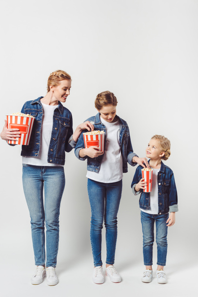 smiling family in similar denim clothing taking popcorn from each other isolated on grey - Photo, Image