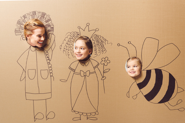 partial view of smiling mother and daughters with heads in cardboard paper with pictures - Photo, Image