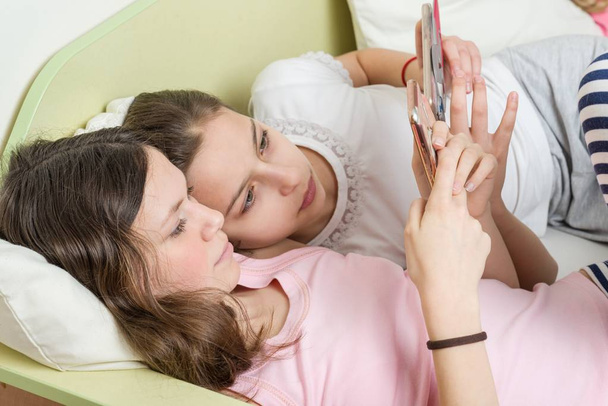 Girls teenagers with interest watch their favorite teen TV series on their smartphone. Lie in bed at home in his room - Φωτογραφία, εικόνα