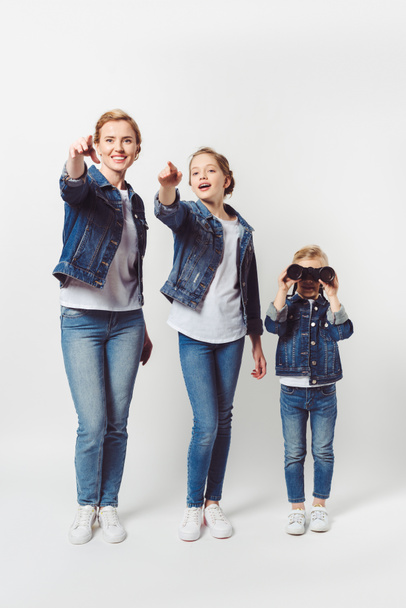 daughter and mother pointing away while little sister with binoculars looking away isolated on grey - Foto, afbeelding