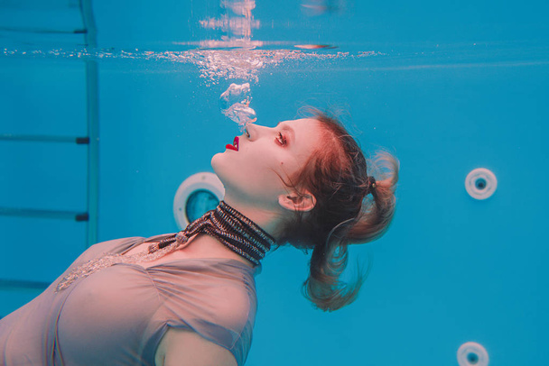 Amazing beautiful art surreal portrait of young woman in grey dress and beaded scarf underwater in the swimming pool - Photo, Image