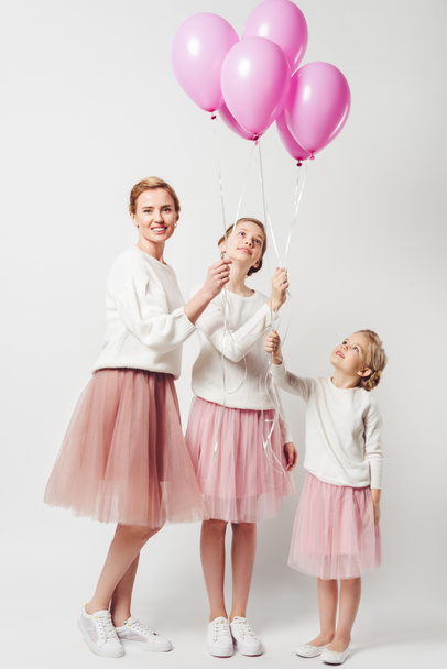 smiling mother and daughter in similar clothing with pink balloons isolated on grey - 写真・画像
