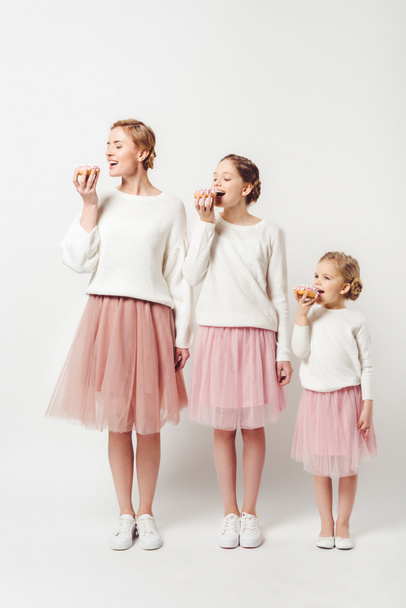 family in similar clothing eating sweet doughnuts isolated on grey - Photo, Image